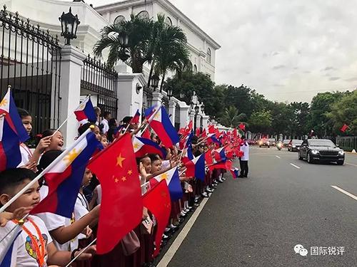 20日，来自马尼拉当地三所小学的千名小学生站在总统府道路两侧挥舞两国国旗，欢迎习主席车队。（图片来源：中央广播电视总台央视新闻 记者邓雪梅拍摄）